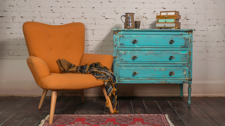 A shabby-chic patinated teal dresser next to an orange armchair