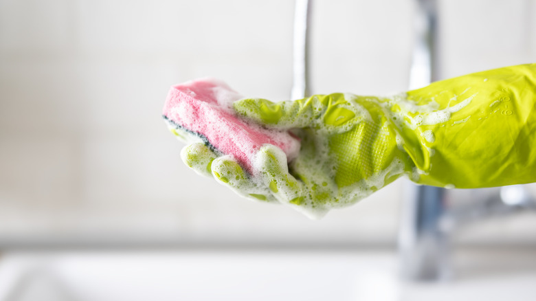 Person wearing rubber gloves with a soapy sponge