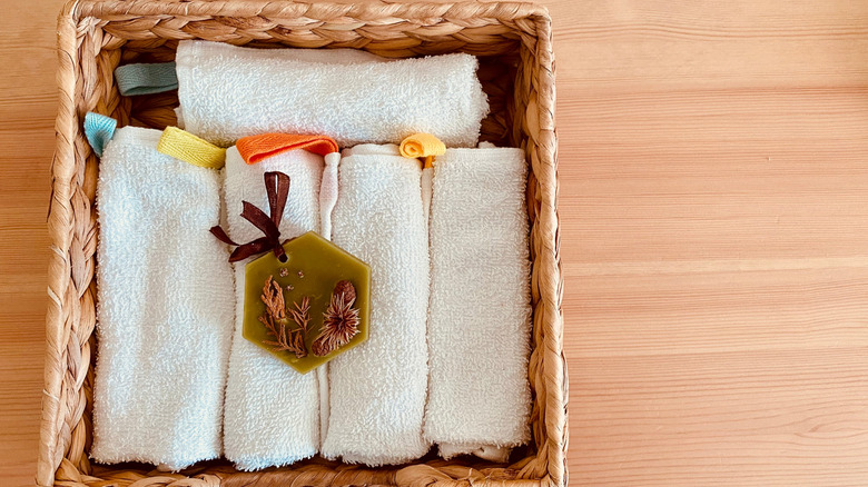 A basket holds several white folded towels, topped with a beeswax sachet
