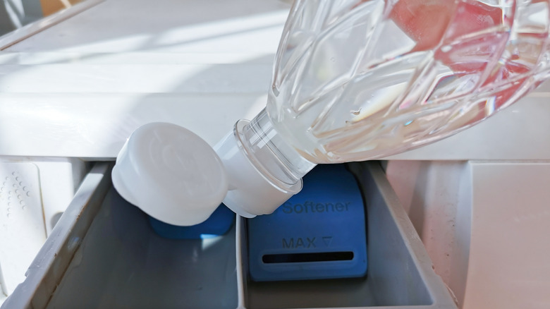 A closeup of a bottle pouring white vinegar into a washing machine