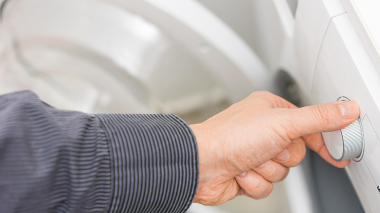 An arm is adjusting washing machine's temperature setting