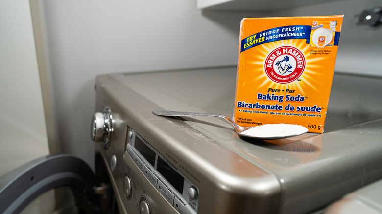 A large box of Arm & Hammer baking soda and a spoon with baking soda on it sitting on top of a washing machine