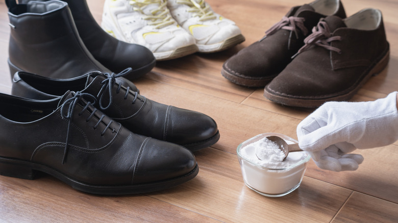 Gloved hand scooping up baking soda with several pairs of shoes around