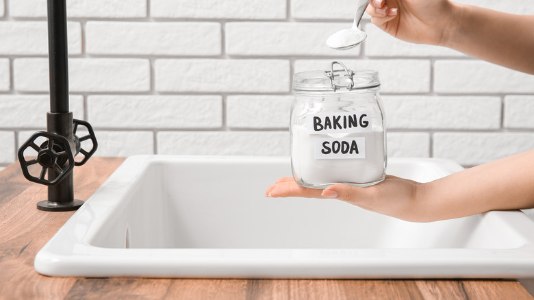 Person scooping baking soda out of a glass container to put into a sink drain