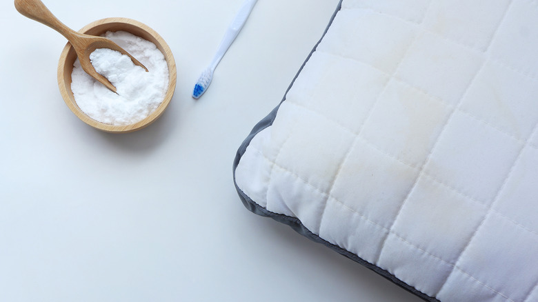 Bowl of baking soda and a toothbrush on a mattress next to a pillow