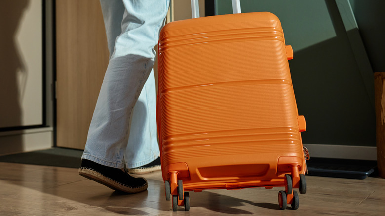 An orange suitcase being pulled by a traveler