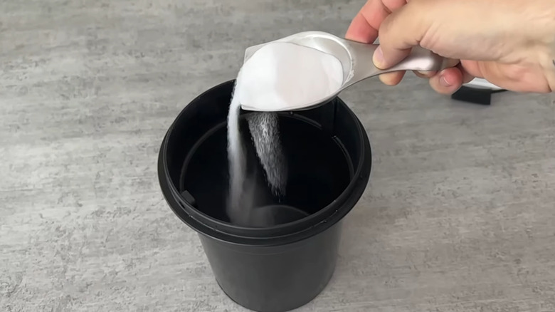 Person sprinkling baking soda into the bottom of a trash bin using a metal scoop
