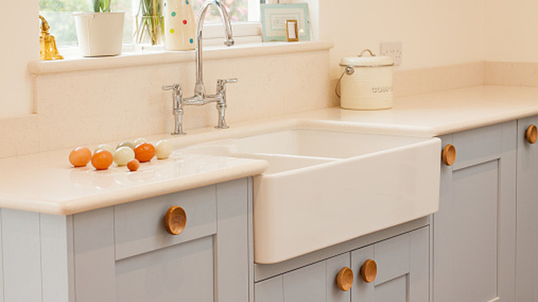 White farmhouse-style sink installed in light painted kitchen cabinets