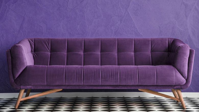 A purple-painted room with a purple couch and black and white floor