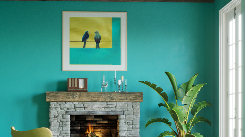 A aqua wall with bird painting above fireplace.