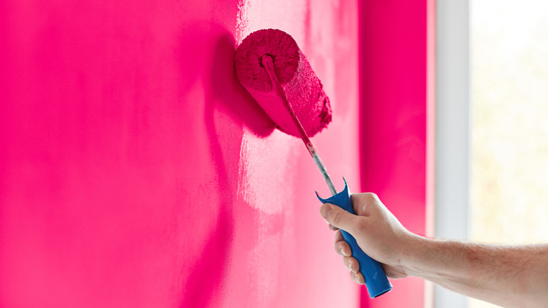 A man's hand uses a roller to paint a room hot pink