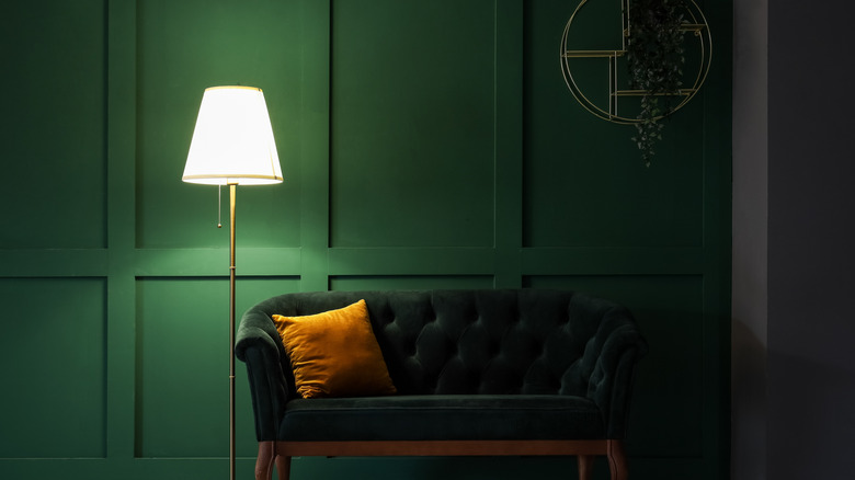 A forest green wall behind a couch and lamp.
