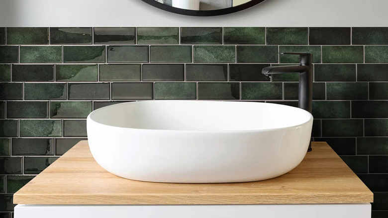Green subway tile backsplash behind modern bathroom sink basin