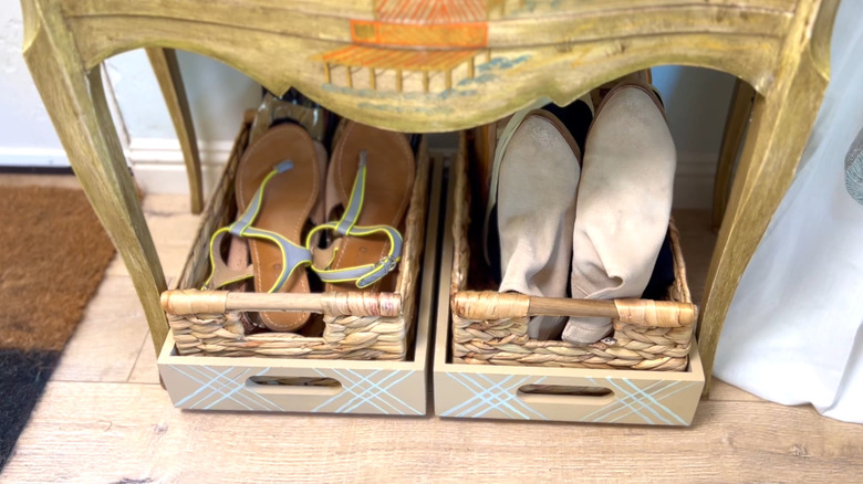 Two trays with baskets in them filled with shoes and tucked under a cabinet