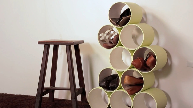 Large pieces of PVC pipe stacked and glued together to create shoe storage in a hallway next to a stool