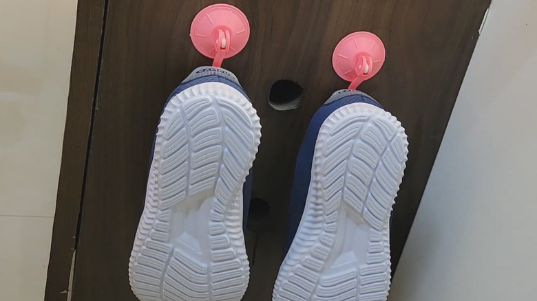 A pair of tennis shoes hanging on the side of a cabinet on suction cup hooks
