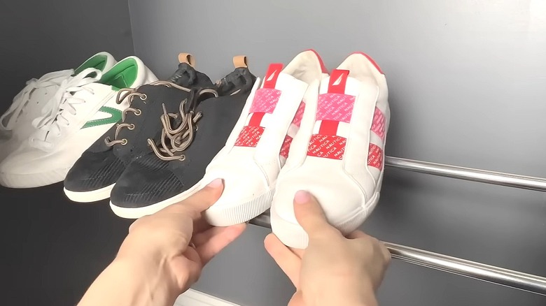 Person putting a pair of tennis shoes on a tension bar rack in a closet