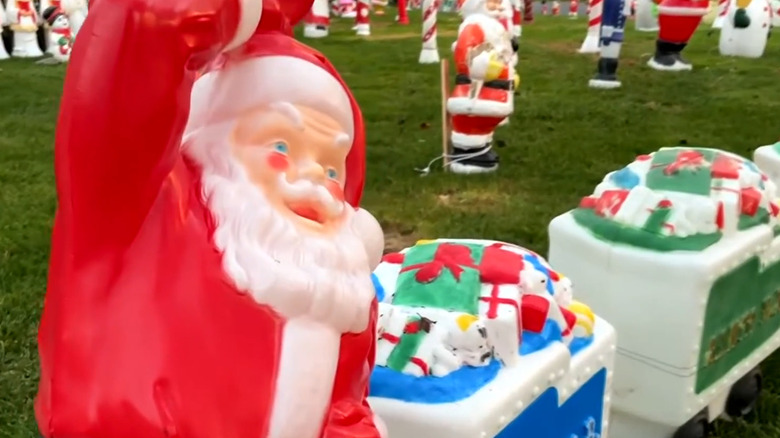 Vintage blow molds in a yard, including Santa's and a present-filled train
