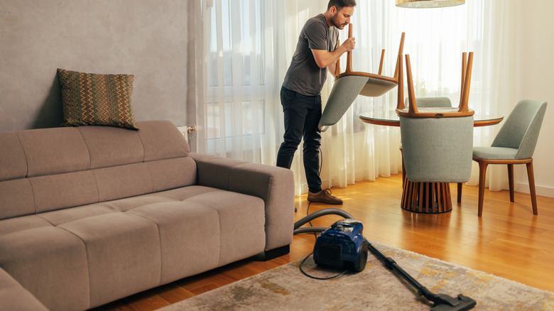 A person preparing a room to vacuum hardwood floors