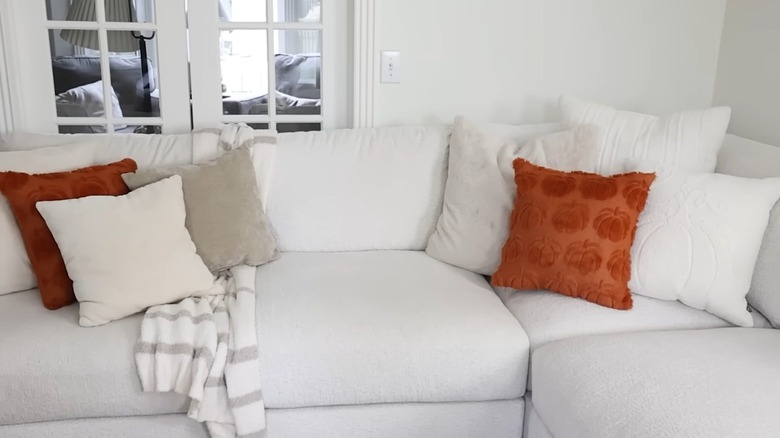 Throw pillows in orange, white, and gray on a white porch sofa