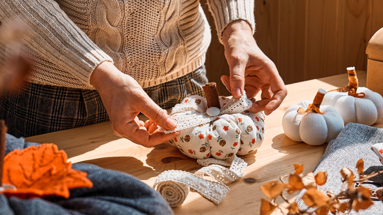 Woman's hands holding decorative bow over a fabric pumpkin
