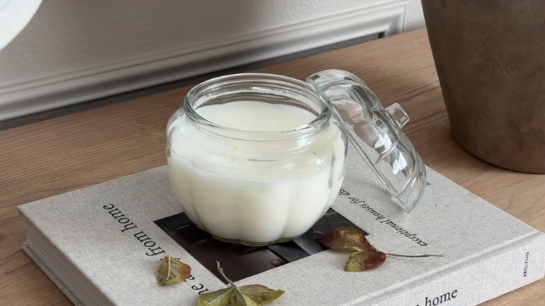 A white wax candle in a pumpkin-shaped glass jar