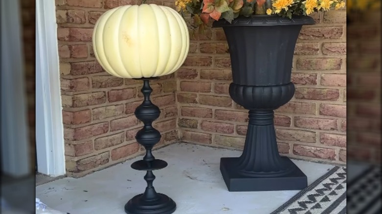 A white foam pumpkin on a black pedestal on porch