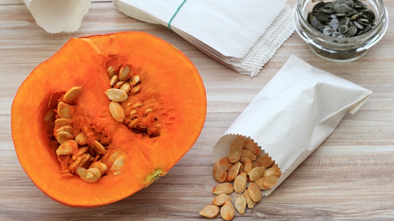 A halved winter squash sits next to an envelope of seeds.