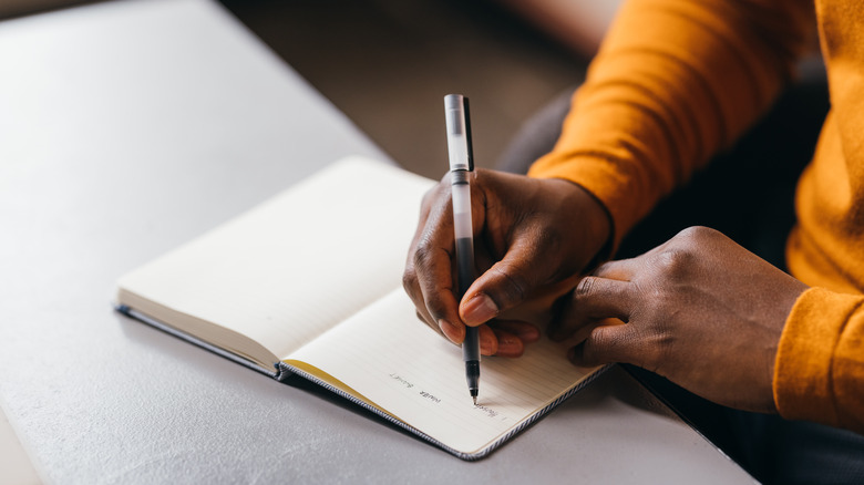A pair of dark-skinned hands with a pen and blank journal