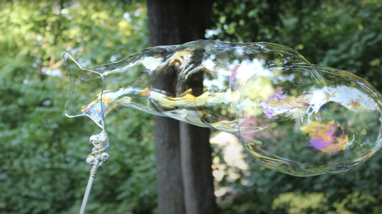 A giant bubble streams out of a bubble wand made from a wire clothes hanger.