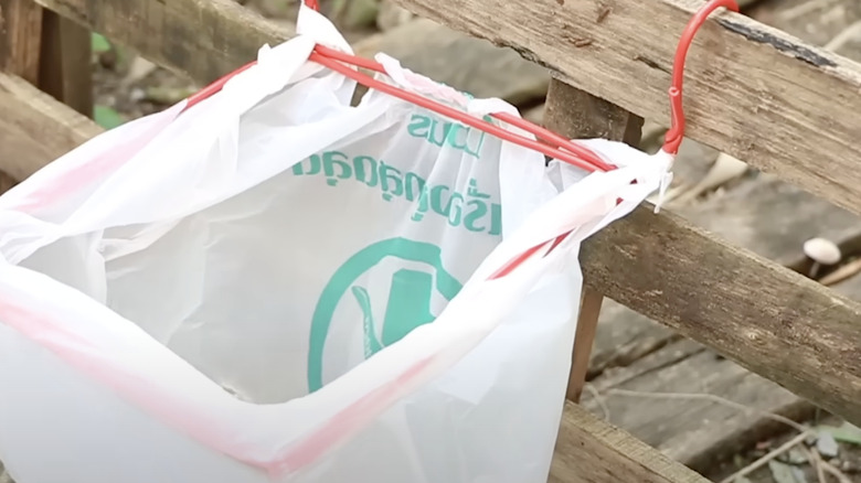 A yard waste bag is held off the ground by a holder made from a wire clothes hanger.