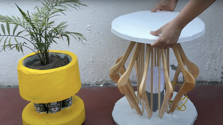 A side table with legs made from wooden clothes hangers sits on a patio beside a yellow concrete planter.