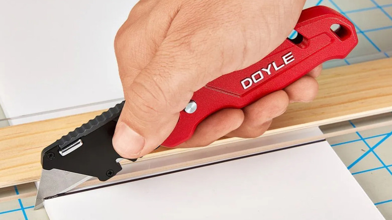 Hand using red Doyle utility knife on work station