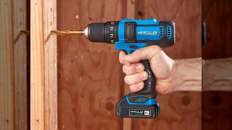 Hand using blue HERCULES compact drill on wood beams
