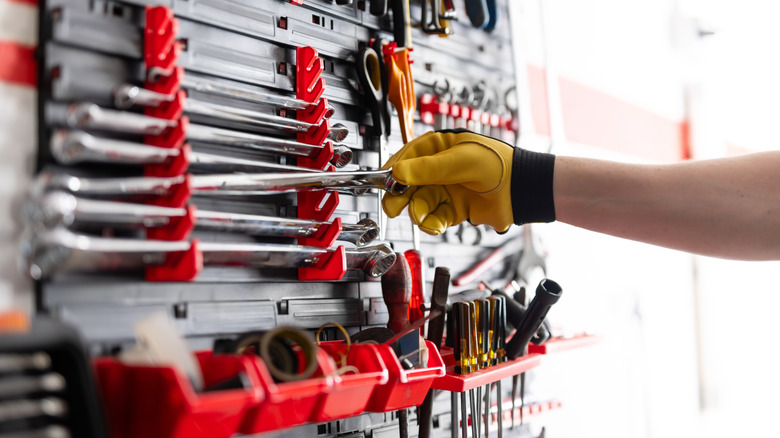 Gloved hand reaching for wrench in tool rack