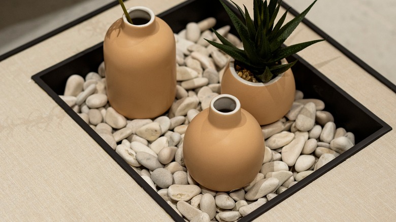 Three vases sitting on a bed of pebbles in a tray on a counter.