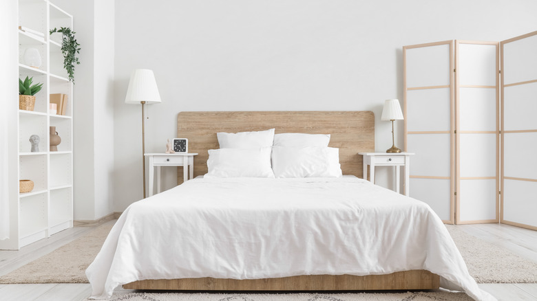 Bedroom with white bed, white folding screen in corner, and a bookshelf