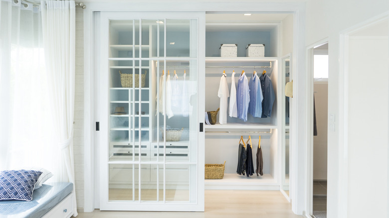Opened glass panel sliding closet doors showing neatly hung clothing