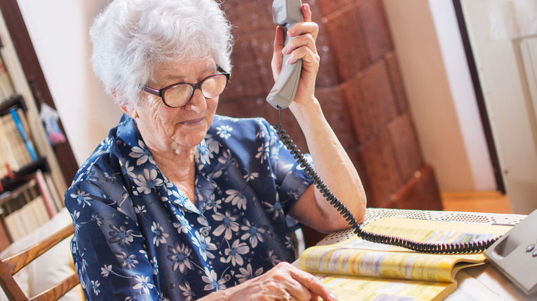 Senior looking up phone number in Yellow Pages and making phone call