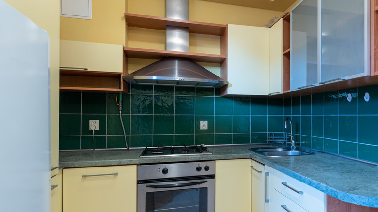 dark teal tile backsplash in kitchen with yellow cabinets