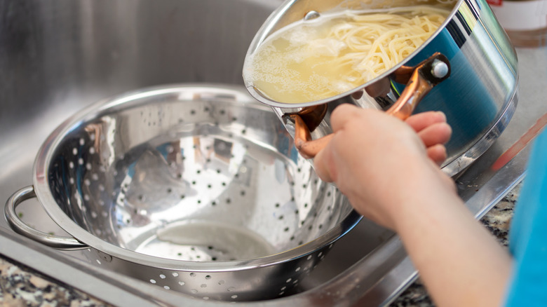 A person straining pasta in a large colander