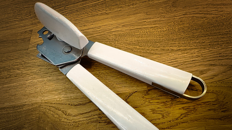 A white-handled manual can opener on a wooden countertop