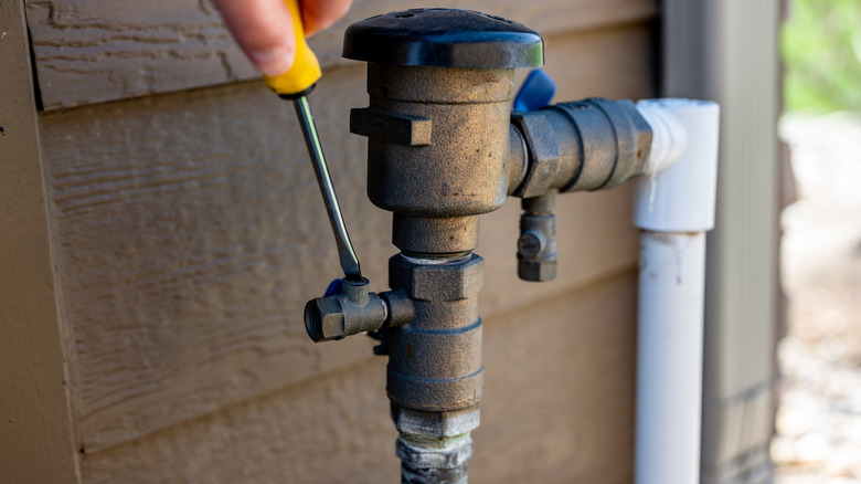 Person using a screwdriver to adjust a pipe valve