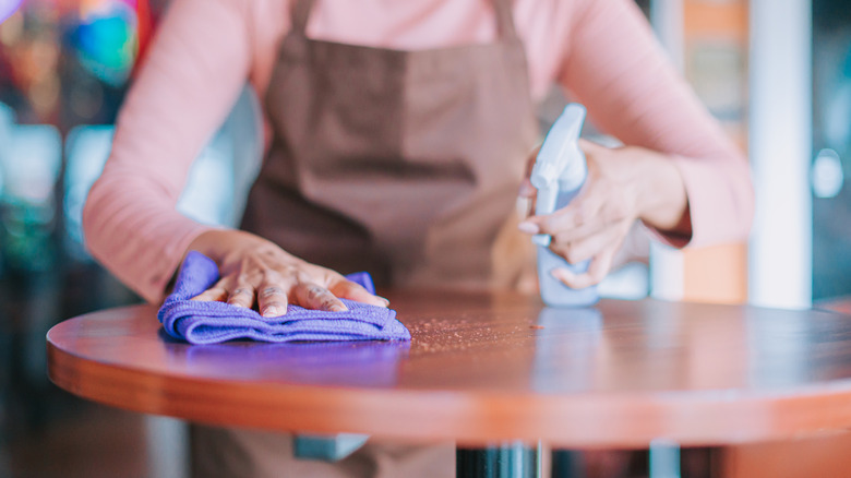 Woman cleaning wood table with a cloth and a cleaner