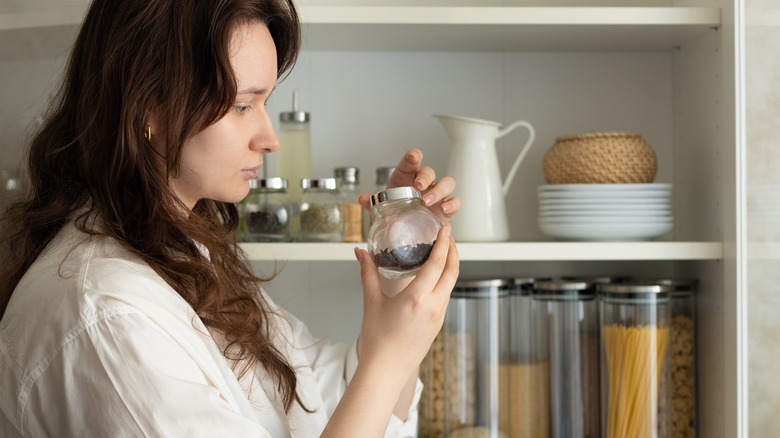 Woman inspecting a jar of cloves, with a stocked pantry shelf in the background