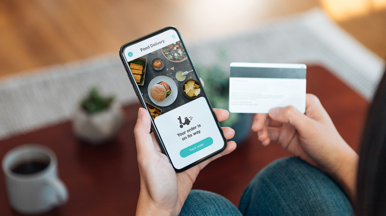 Over-the-shoulder view of someone completing a takeout food order on their phone, holding a credit card in the other hand