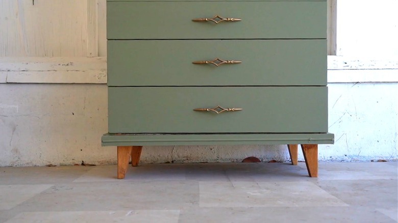 A green dresser with mid century furniture legs.