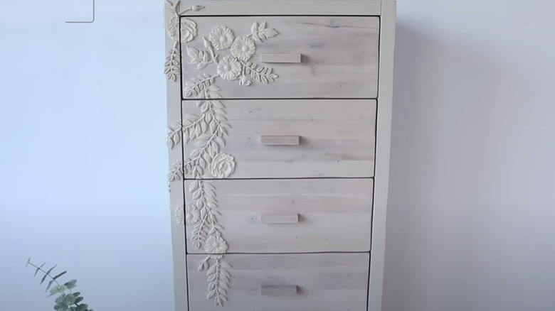 A tall dresser with carved flower appliques.
