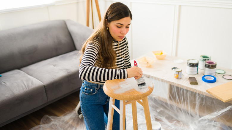 A girl in a striped shift painting a stool.