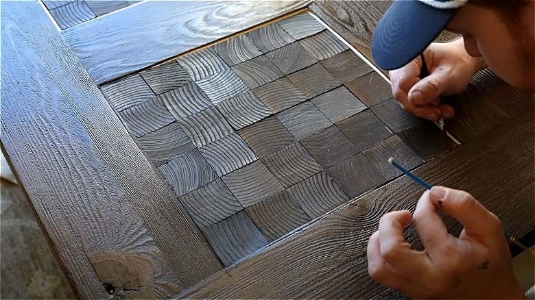 A man painting the edge of a wood coffee table.